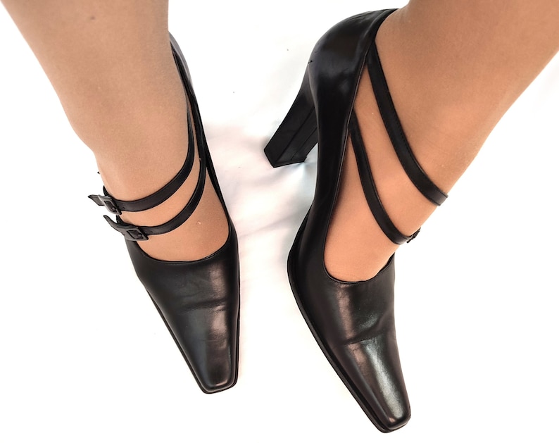 May include: A pair of black leather heeled shoes with a pointed toe and double straps with buckles. The shoes have a chunky heel.