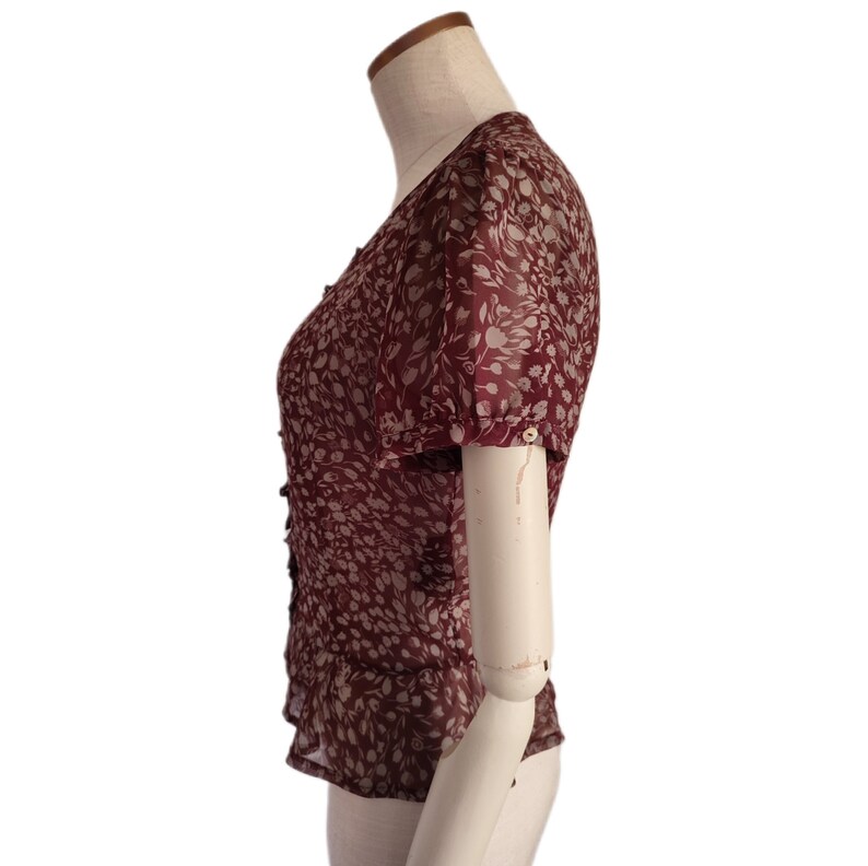 May include: A maroon blouse with a floral print and short sleeves. The blouse has a button-up front and a ruffled hem.