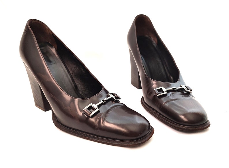 May include: A pair of brown leather heeled pumps with a silver buckle detail.