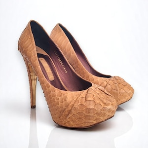May include: A pair of tan snakeskin high-heeled pumps with gold heels. The shoes have a platform sole and a pointed toe.