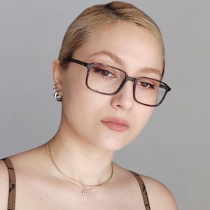 May include: A woman with blonde hair wearing brown square-shaped glasses and a gold necklace.