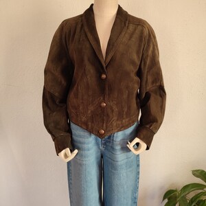 Puede incluir: Una chaqueta de ante marr&oacute;n con cuello y cierre de botones. La chaqueta tiene mangas largas con pu&ntilde;os.