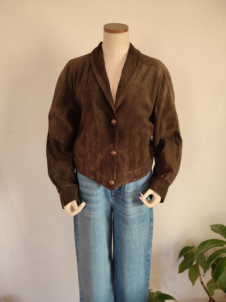 Puede incluir: Una chaqueta de ante marr&oacute;n con cuello y cierre de botones. La chaqueta tiene mangas largas con pu&ntilde;os.