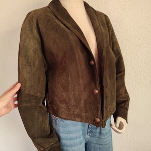 Puede incluir: Una chaqueta de ante marr&oacute;n con cuello y cierre de botones. La chaqueta tiene mangas largas y un dobladillo recortado.