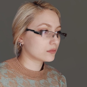 Può includere: Una donna con i capelli biondi indossa occhiali con montatura marrone e nera. Gli occhiali hanno la parola "polarizzato" stampata sulla lente destra. Indossa un maglione con motivo marrone e blu.