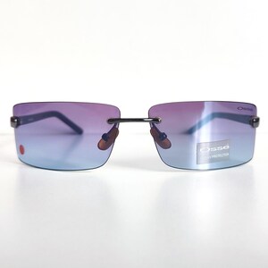 May include: Rimless sunglasses with a gradient lens, shifting from purple to blue. The sunglasses have a black frame and the brand name "Osse" is visible on the lens. A small red dot is on the left lens.