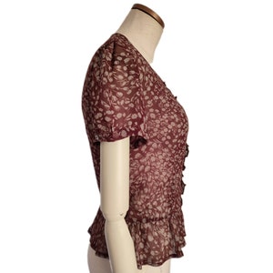 May include: A maroon blouse with a white floral print and a ruffled hem. The blouse has short sleeves and a V-neck.