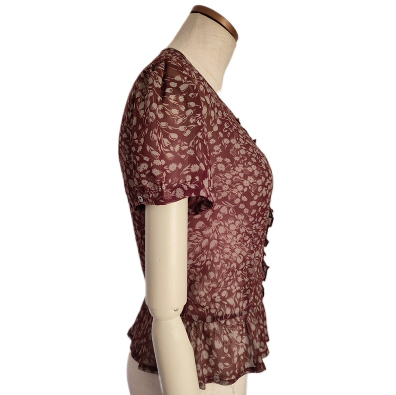 May include: A maroon blouse with a white floral print and a ruffled hem. The blouse has short sleeves and a V-neck.