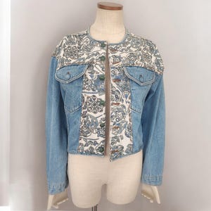 May include: A blue denim jacket with a white and blue patterned fabric overlay. The jacket has a button closure and two pockets.
