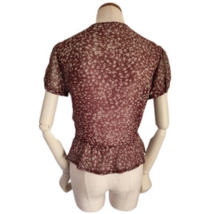 May include: A maroon blouse with a white floral print. The blouse has a ruffled neckline and short sleeves.