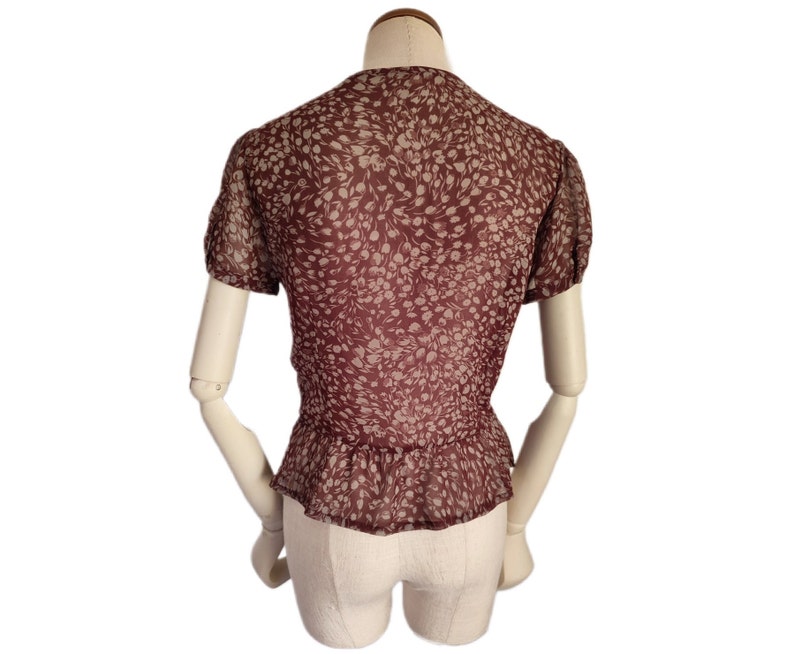 May include: A maroon blouse with a white floral print. The blouse has a ruffled neckline and short sleeves.