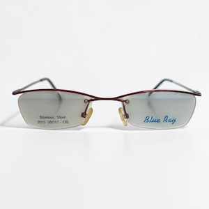 May include: Semi-rimless spectacles with a thin dark red metal frame and clear lenses. The left lens features the blue text "Blue Ray" and the right lens displays "Stainless Steel 2015 50□17-135" in black. The glasses include gold-toned nose pads.