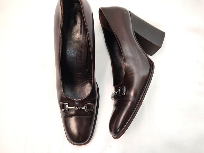 May include: A pair of brown leather heeled pumps with a silver buckle detail. The shoes have a square toe and a chunky heel.