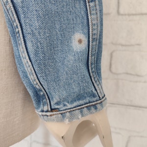 Pu&ograve; includere: Primo piano della manica in denim blu chiaro di una giacca. La manica presenta una piccola macchia marrone.