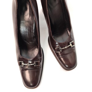May include: A pair of brown leather heeled shoes with silver buckles. The shoes have a pointed toe and a closed back.