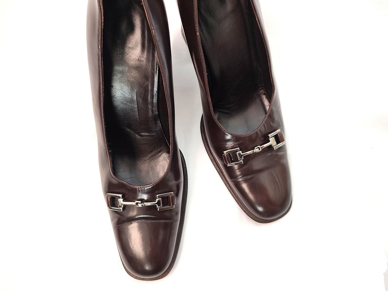May include: A pair of brown leather heeled shoes with silver buckles. The shoes have a pointed toe and a closed back.