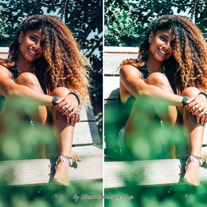 May include: A woman with long curly brown hair sits on a wooden bench with green foliage in the foreground. She is wearing a black tank top and a silver necklace. She is smiling and looking at the camera.