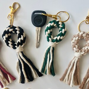 Może przedstawiać: Pięć breloków z frędzlami w różnych kolorach. Frędzle są wykonane z plecionego sznurka i mają pierścień na górze. Breloki są przymocowane do złotych metalowych kółek.