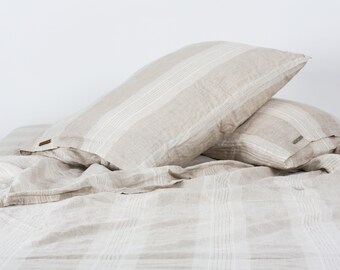 Puede incluir: Dos fundas de almohada de lino beige con rayas blancas están dobladas sobre una sábana de lino beige con rayas blancas.
