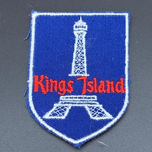 May include: A shield-shaped embroidered patch with a blue background and a white border. It features a white stitched outline of a tower structure and the red embroidered text Kings Island centered across the middle of the design.