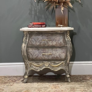May include: A distressed grey and gold bedside table with two drawers and a white marble top. The table has ornate carvings and a decorative design on the front.
