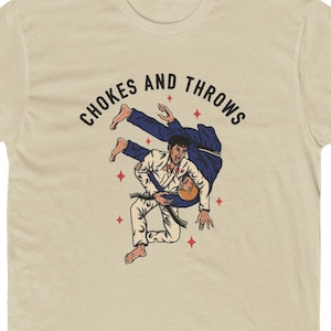 May include: A beige t-shirt featuring a graphic of two people in a martial arts chokehold. The text "Chokes and Throws" is printed in black above the graphic.