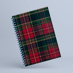 May include: A spiral-bound notebook featuring a classic plaid pattern in red, green, yellow, and brown. The notebook has a blue spiral binding and a hard cover. The plaid design is a traditional tartan pattern.