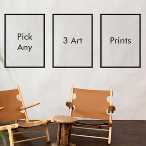 May include: Three framed art prints with black borders hang on a white wall. The prints read "Pick Any", "3 Art", and "Prints". Two wooden chairs with tan leather seats and a small wooden side table are in front of the wall.