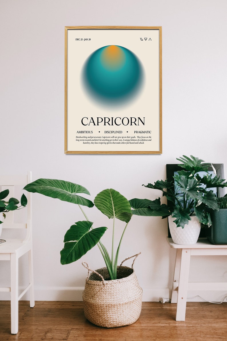 May include: A framed Capricorn zodiac sign art print. The artwork features a teal and orange sphere on a cream background, with the word "CAPRICORN" and related traits below. The print is displayed in a room with plants.