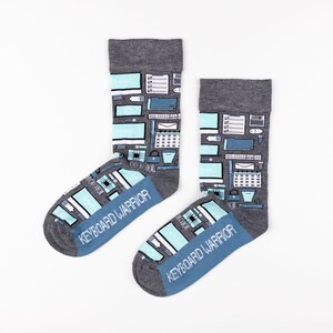 May include: A pair of gray socks with a blue and white pattern of office supplies and the text "Keyboard Warrior".