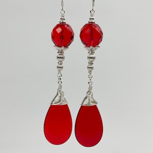 May include: A pair of long, silver earrings with red teardrop-shaped glass beads and faceted round glass beads.