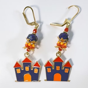 May include: A pair of gold-tone dangle earrings. Each earring features a blue castle charm with orange and red accents, and a beaded cluster of red, orange, and blue beads. The earrings have lever-back closures.