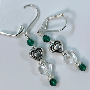 May include: Silver earrings with a heart charm and green and clear crystal beads.