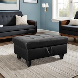 May include: Black rectangular ottoman with a tufted top and four short legs. The ottoman has a storage compartment with a handle. It is placed on a light-colored rug in a living room setting. The room also features a sofa and chairs.