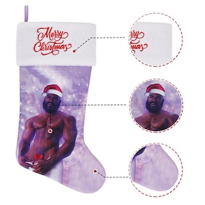 May include: A purple and white Christmas stocking with a festive design. The stocking features a man wearing a Santa hat and a bow tie. The stocking has the words "Merry Christmas" embroidered on the cuff.