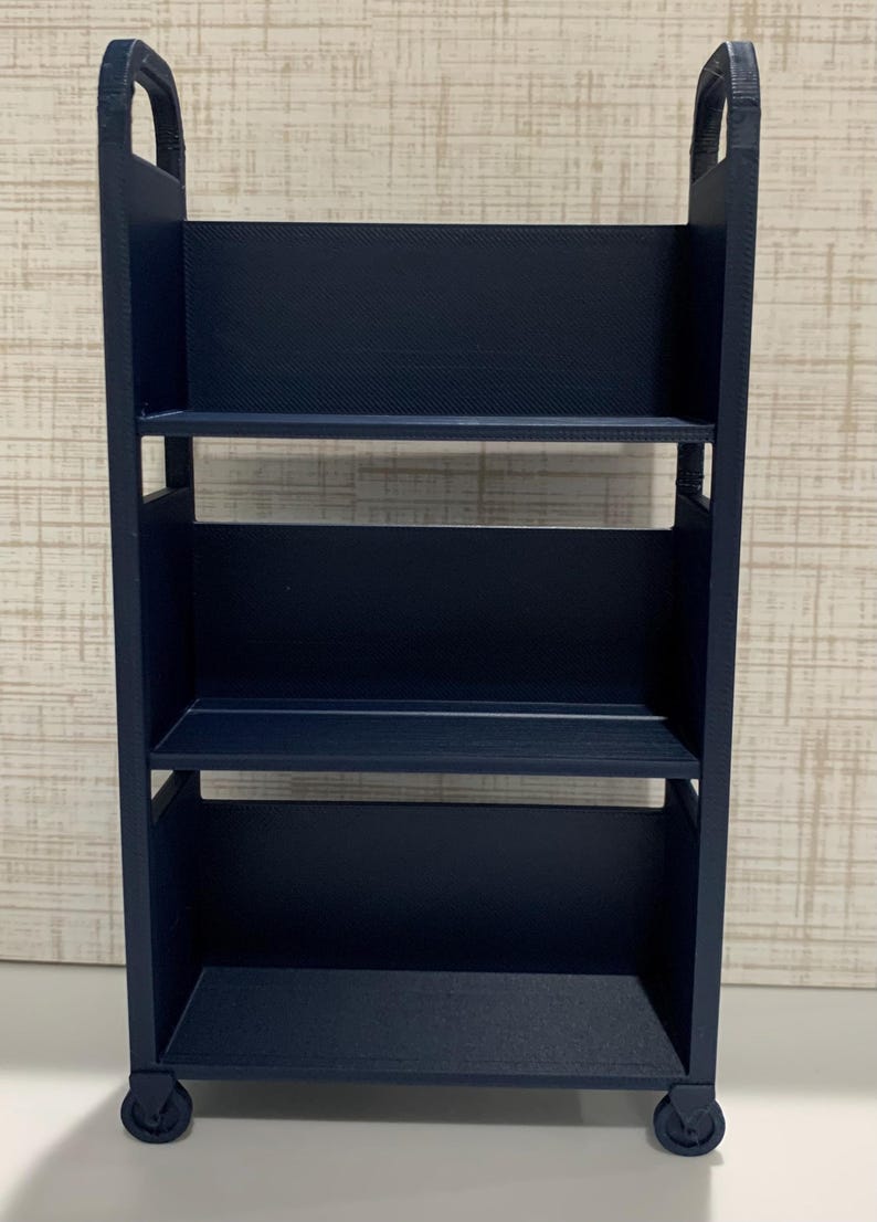 May include: A dark navy blue three-tiered rolling cart featuring a rectangular frame with two vertical side panels, integrated handles at the top, and four small wheels at the base. The unit has three open shelves with solid back panels.
