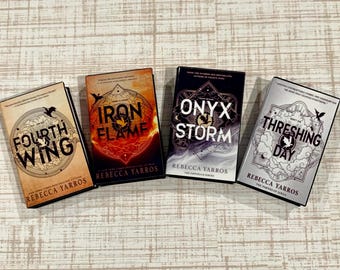 May include: Four books by Rebecca Yarros from The Empyrean Series arranged in a row. The titles are Fourth Wing with a tan cover, Iron Flame with an orange cover, Onyx Storm with a black cover, and Threshing Day with a silver cover.