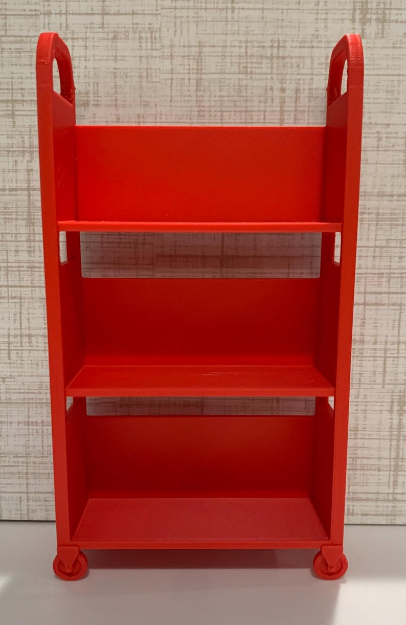 May include: A bright red, three-tiered rolling utility cart featuring a rectangular frame with integrated handles at the top and four small wheels at the base. The cart has three open shelves for storage and a smooth, matte finish throughout.
