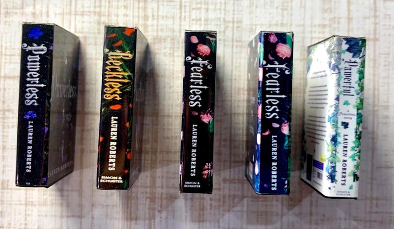May include: Five hardcover books by Lauren Roberts are displayed. The spines feature titles like "Powerless," "Reckless," and "Fearless," with floral and abstract designs. The books are in various colors, including black, blue, and white.