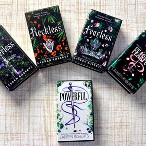 May include: Five books with dark covers are arranged on a light wood-grain surface. The book titles are "Powerless", "Reckless", "Fearless", "Fearful", and "Powerful". Each book has the author's name, Lauren Roberts, printed on the cover.