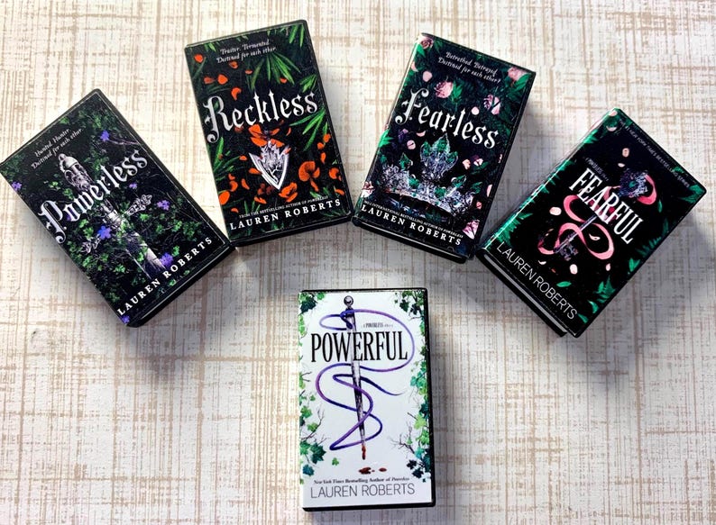May include: Five books with dark covers are arranged on a light wood-grain surface. The book titles are "Powerless", "Reckless", "Fearless", "Fearful", and "Powerful". Each book has the author's name, Lauren Roberts, printed on the cover.