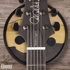 Electric guitar headstock resting on ebony wood guitar wall hanger with circular hardwood base and padded arms
