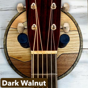 Acoustic guitar headstock on dark walnut wood wall mount guitar hanger with round layered hardwood backplate and padded arms