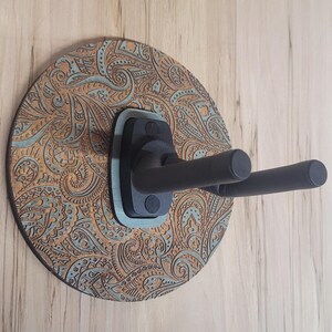 Side profile of a guitar hanger showing the "Wildwood Guitar Hangers" logo engraved on the side of a teal-stained wooden accent piece.