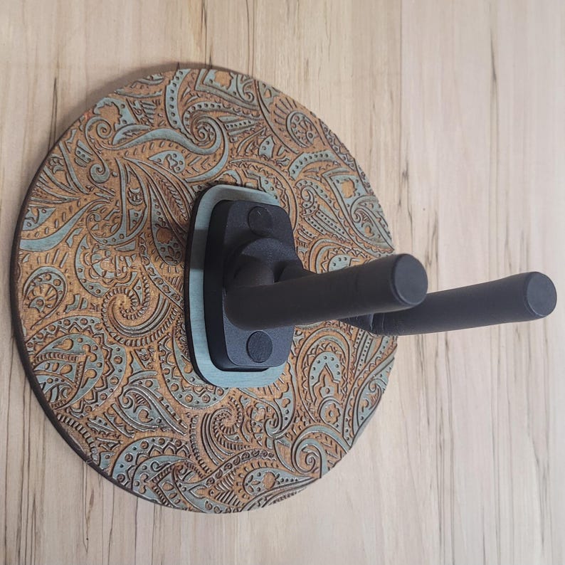 Side profile of a guitar hanger showing the "Wildwood Guitar Hangers" logo engraved on the side of a teal-stained wooden accent piece.