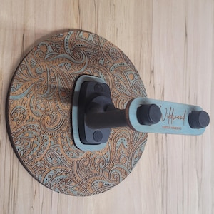 Side profile of a guitar hanger showing the "Wildwood Guitar Hangers" logo engraved on the side of a teal-stained wooden accent piece.