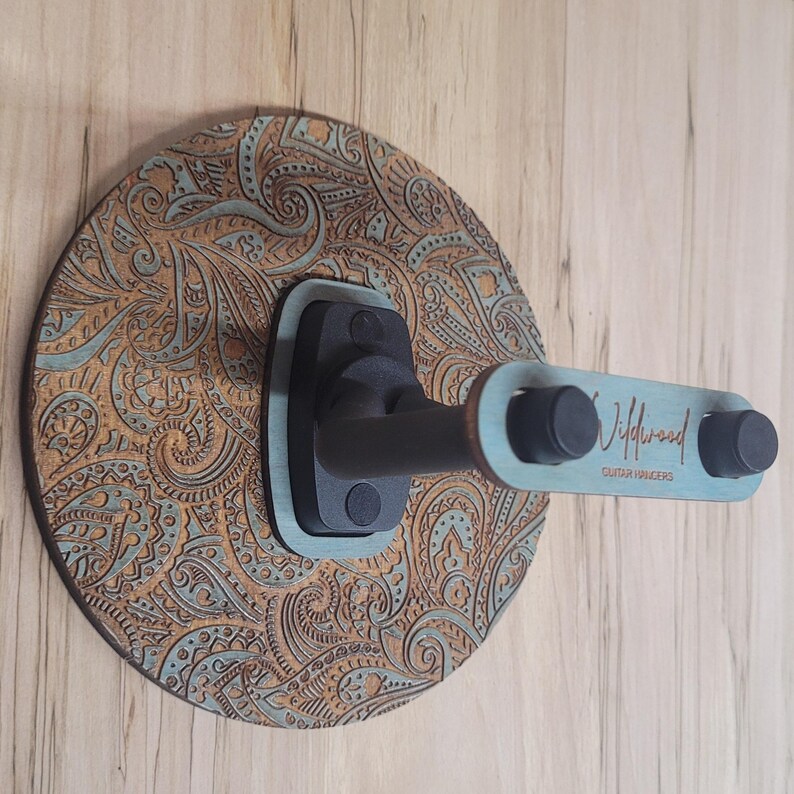 Side profile of a guitar hanger showing the "Wildwood Guitar Hangers" logo engraved on the side of a teal-stained wooden accent piece.