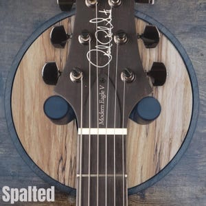 Acoustic guitar headstock resting on spalted wood wall mount guitar hanger with padded arms and round hardwood backplate