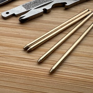 Könnte beinhalten: Vier goldfarbene Metallstäbe mit spitzen Enden. Die Stäbe sind in einer Reihe angeordnet, wobei die Spitzen der Stäbe nach rechts zeigen.