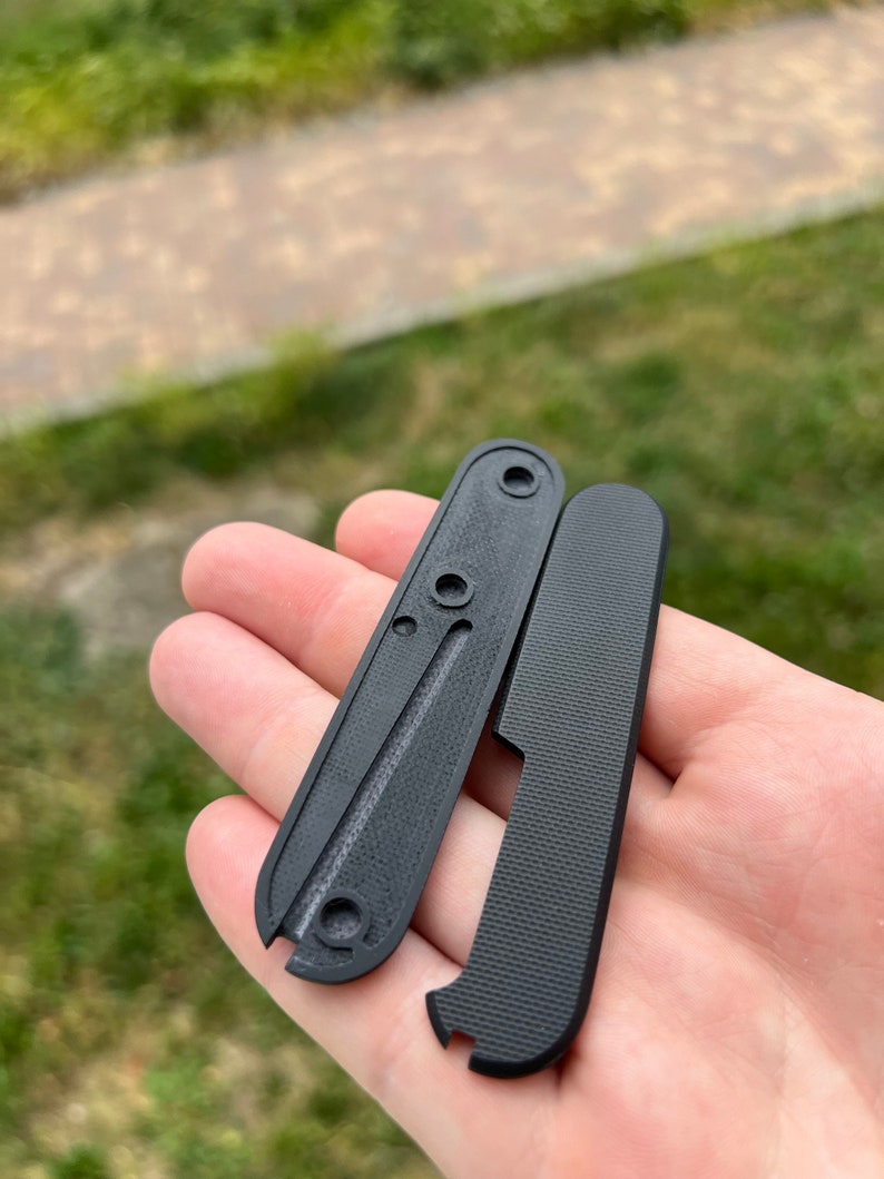 May include: Two black plastic scales for a pocket knife. The scales have a textured surface and are designed to fit a specific knife model.
